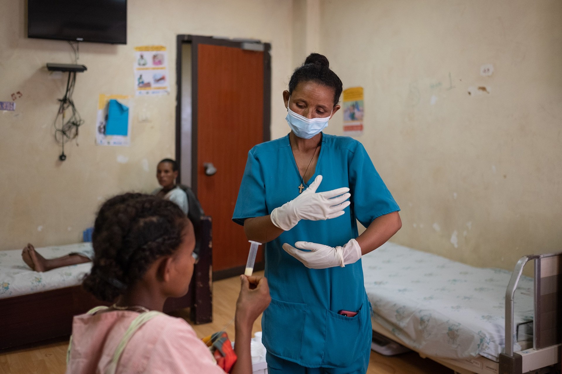 Photo of one person sitting at a desk with another person looking over their shoulder to review something on the desktop screen at a hospital in South Sudan.