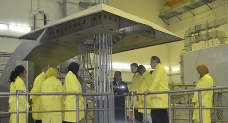 9 people wearing yellow protective suits, gathering by a machine in the National Nuclear Energy Agency facility.